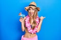 Young blonde girl wearing bikini and hawaiian lei drinking cocktail pointing thumb up to the side smiling happy with open mouth Royalty Free Stock Photo