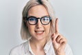 Young blonde girl wearing casual clothes and glasses smiling with an idea or question pointing finger with happy face, number one Royalty Free Stock Photo