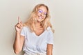 Young blonde girl wearing casual clothes and glasses smiling with an idea or question pointing finger up with happy face, number Royalty Free Stock Photo