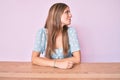 Young blonde girl wearing casual clothes sitting on the table looking to side, relax profile pose with natural face with confident Royalty Free Stock Photo