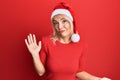 Young blonde girl wearing christmas hat clueless and confused expression with arms and hands raised Royalty Free Stock Photo