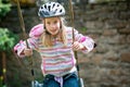 A young blonde girl wearing a cycle helmet while swinging on a garden swing