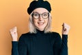 Young blonde girl wearing french look with beret celebrating surprised and amazed for success with arms raised and open eyes