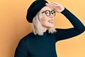 Young blonde girl wearing french look with beret very happy and smiling looking far away with hand over head Royalty Free Stock Photo