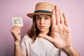 Young blonde girl wearing a hat holding paper note with yes word as positive message with open hand doing stop sign with serious Royalty Free Stock Photo