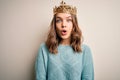 Young blonde girl wearing queen golden crown over isolated background afraid and shocked with surprise expression, fear and Royalty Free Stock Photo