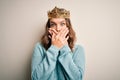 Young blonde girl wearing queen golden crown over isolated background shocked covering mouth with hands for mistake Royalty Free Stock Photo