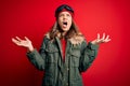 Young blonde girl wearing ski glasses and winter coat for ski weather over red background crazy and mad shouting and yelling with Royalty Free Stock Photo