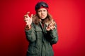 Young blonde girl wearing ski glasses and winter coat for ski weather over red background Shouting frustrated with rage, hands Royalty Free Stock Photo