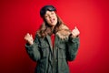 Young blonde girl wearing ski glasses and winter coat for ski weather over red background very happy and excited doing winner