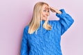 Young blonde girl wearing wool winter sweater very happy and smiling looking far away with hand over head Royalty Free Stock Photo