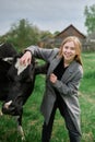 young blonde happy girl in coat hugs the cow in the green field Royalty Free Stock Photo