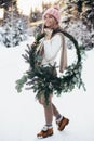 Blonde young lady with christmas wreath in winter forest