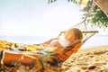 Young blonde longhaired woman relaxing in hammock hinged between palm trees on the sand beach Royalty Free Stock Photo