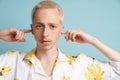 Young blonde man looking at camera while plugging his ears Royalty Free Stock Photo