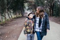 Young blonde mother walking and talking with her young son in a park road. Single parent family Royalty Free Stock Photo