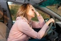 A young blonde nervous woman is sitting behind the wheel of a left-hand drive car and holding her head. Side view. Fine Royalty Free Stock Photo