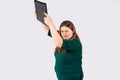 Young blonde overwight businesswoman in green dress over gray background, frustrated large woman holding pc computer up Royalty Free Stock Photo