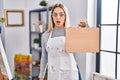 Young blonde painter woman holding wooden case at art studio scared and amazed with open mouth for surprise, disbelief face Royalty Free Stock Photo