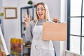 Young blonde painter woman holding wooden case at art studio smiling happy pointing with hand and finger to the side Royalty Free Stock Photo