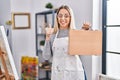 Young blonde painter woman holding wooden case at art studio smiling happy and positive, thumb up doing excellent and approval Royalty Free Stock Photo