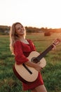 Young blonde plays guitar and smiles in a field at sunset. Royalty Free Stock Photo