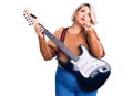 Young blonde plus size woman playing electric guitar serious face thinking about question with hand on chin, thoughtful about Royalty Free Stock Photo