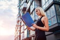 Young blonde real eastate agent reading contract by modern multi-storey building in city. Businesswoman examines project Royalty Free Stock Photo