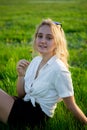 A young blonde is sitting in a clearing and holding a dandelion. Green grass. Royalty Free Stock Photo