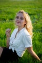 A young blonde is sitting in a clearing and holding a dandelion. Green grass. Royalty Free Stock Photo