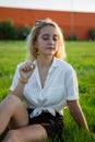 A young blonde is sitting in a clearing and holding a dandelion. Green grass. Royalty Free Stock Photo