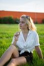 A young blonde is sitting in a clearing and holding a dandelion. Green grass. Royalty Free Stock Photo