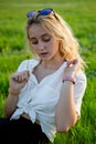 A young blonde is sitting in a clearing and holding a dandelion. Green grass. Royalty Free Stock Photo