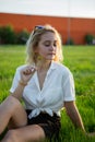 A young blonde is sitting in a clearing and holding a dandelion. Green grass. Royalty Free Stock Photo