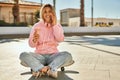 Young blonde skater girl talking on the smartphone and drinking coffee at the park Royalty Free Stock Photo