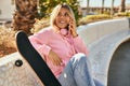 Young blonde skater girl talking on the smartphone and using headphones at the park Royalty Free Stock Photo