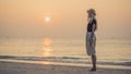 Young blonde stands on the shore of the morning sea and looking at the camera. Walking barefoot on the beach. Royalty Free Stock Photo