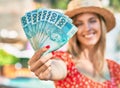 Young blonde tourist woman wearing summer style holding brazilian 100 real banknotes at the city