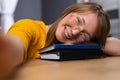 Young blonde, wearing yellow blouse and eyeglasses, taking a selfie, holding her head on the books. Student with black and blue Royalty Free Stock Photo