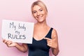 Young blonde woman asking for women freedom holding paper with my body my rules message smiling happy pointing with hand and