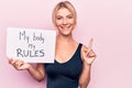 Young blonde woman asking for women freedom holding paper with my body my rules message smiling with an idea or question pointing