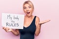 Young blonde woman asking for women freedom holding paper with my body my rules message celebrating achievement with happy smile