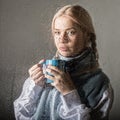 Young blonde woman behind glass with water drops. beautiful girl drinks coffee or tea Royalty Free Stock Photo