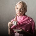 Young blonde woman behind glass with water drops. beautiful girl drinks coffee or tea Royalty Free Stock Photo