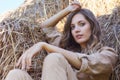 Young blonde woman in a beige jumpsuit is sitting on the rolls of hay Royalty Free Stock Photo