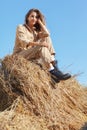 Young blonde woman in a beige jumpsuit is sitting on the rolls of hay Royalty Free Stock Photo