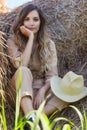 Young blonde woman in a beige jumpsuit is sitting on the rolls of hay Royalty Free Stock Photo