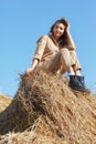 Young blonde woman in a beige jumpsuit is sitting on the rolls of hay Royalty Free Stock Photo