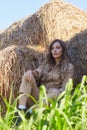 Young blonde woman in a beige jumpsuit is sitting on the rolls of hay Royalty Free Stock Photo