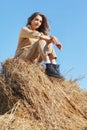 Young blonde woman in a beige jumpsuit is sitting on the rolls of hay Royalty Free Stock Photo